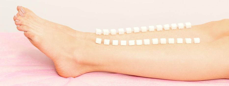 The concept of epilation, waxing. Sugar cubes lie down in a row on the naked white female leg