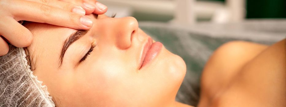 Head massage. Beautiful caucasian young white woman receiving a head and forehead massage with closed eyes in a spa salon