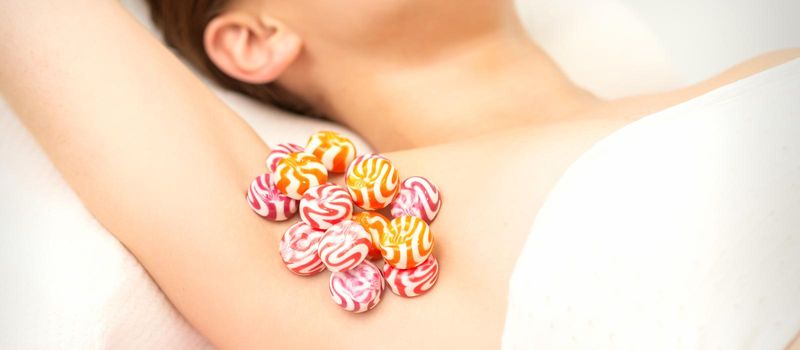 Waxing, depilation armpit concept. Colored round candies lying down on the female armpit, close up