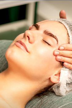 Head massage. Beautiful caucasian young white woman receiving a head and forehead massage with closed eyes in a spa salon