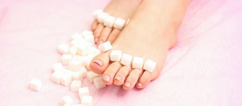 The concept of epilation, waxing. Sugar cubes lying down in a row on female feet, toes over pink background