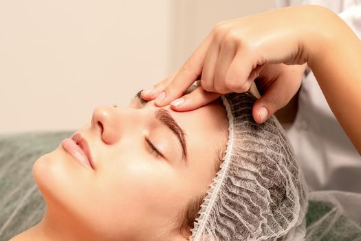 Beautiful caucasian young woman receiving a facial massage with closed eyes in spa salon, close up. Relaxing treatment concept