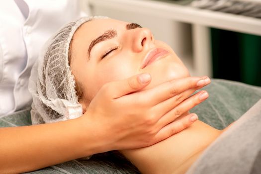 Facial massage. Hands of a masseur massaging neck of a young caucasian woman in a spa salon, the concept of health massage