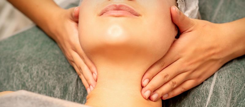 Facial massage. Hands of a masseur massaging neck of a young caucasian woman in a spa salon, the concept of health massage