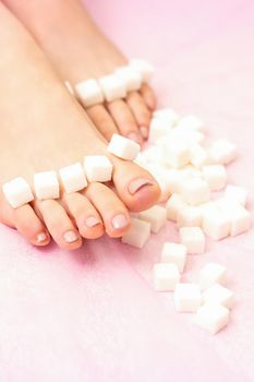 The concept of epilation, waxing. Sugar cubes lying down in a row on female feet, toes over pink background