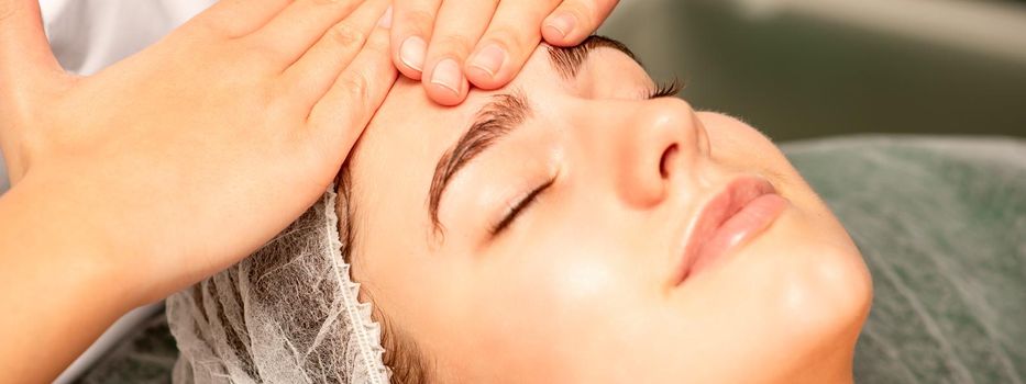 Head massage. Beautiful caucasian young white woman receiving a head and forehead massage with closed eyes in a spa salon