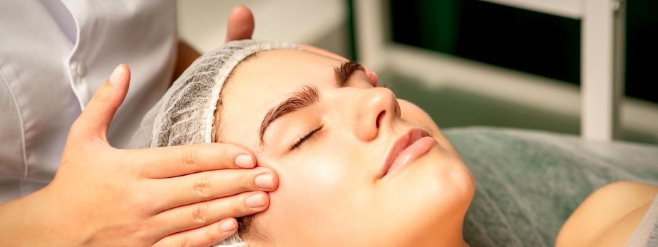 Head massage. Beautiful caucasian young white woman receiving a head and forehead massage with closed eyes in a spa salon