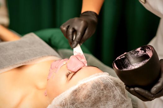 Beautiful young caucasian woman receiving an alginic mask to the face in beauty salon. Facial skin treatment