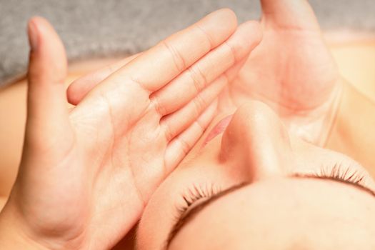 Beautiful caucasian young woman receiving a facial massage with closed eyes in spa salon, close up. Relaxing treatment concept