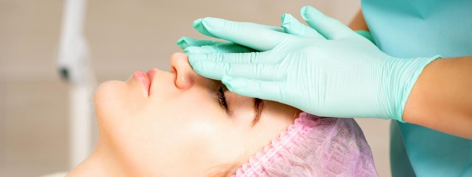 Cosmetologist with gloved hands applies a moisturizing mask with peeling cream on the female face. Facial cosmetology treatment. Procedures for facial care