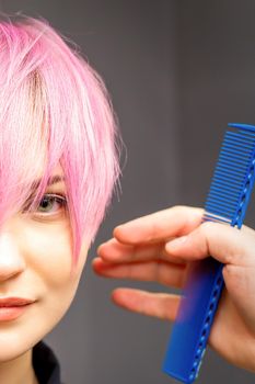 Hairdresser with hands and comb is checking out and fixing the short pink hairstyle of the young white woman in a hair salon