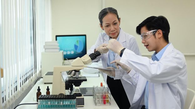 Professional scientists team conducting experiments, consisting of glassware test tubes and microscopes in laboratory.