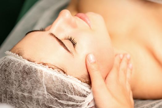 Facial massage. Hands of a masseur massaging neck of a young caucasian woman in a spa salon, the concept of health massage