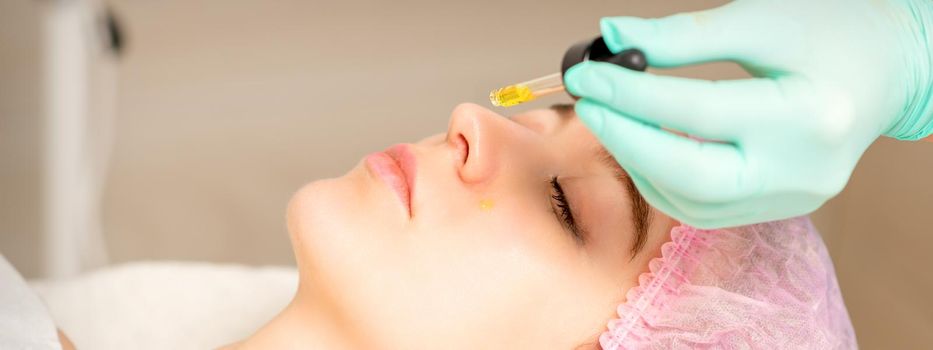 Young white woman getting acid organic retinol peel face skin with the pipette in a beauty clinic