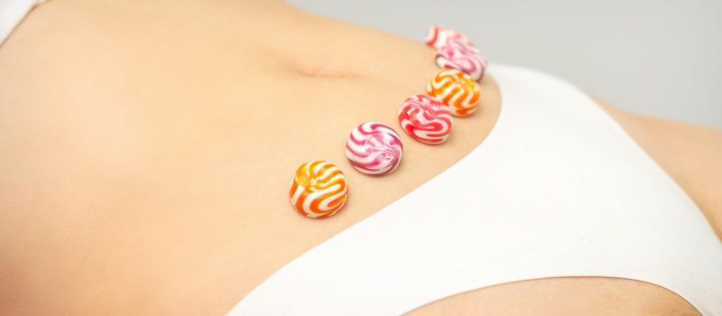 Concept of intimate depilation, intimate waxing, depilation. Round candies lying down in a row on the female bikini zone, intimate area, close up