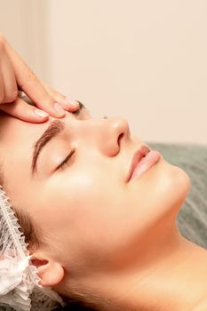 Beautiful caucasian young woman receiving a facial massage with closed eyes in spa salon, close up. Relaxing treatment concept