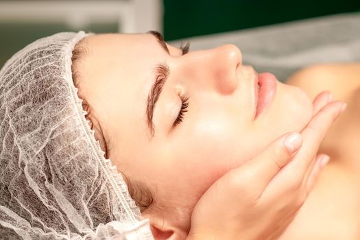 Facial massage. Hands of a masseur massaging neck of a young caucasian woman in a spa salon, the concept of health massage