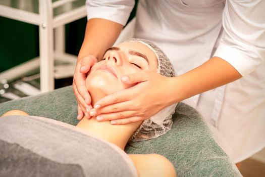 Facial treatment massage. Beautiful young caucasian woman with perfect skin receiving face and neck massage at a beauty spa