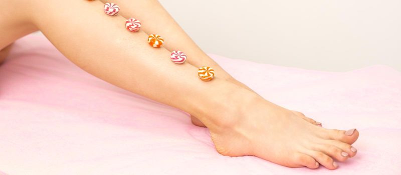 Depilation, waxing concept. Round candies lying down in a row on the female leg, close up