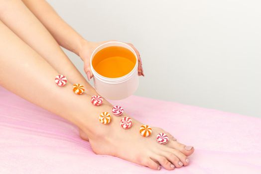 Depilation, waxing concept. Round candies lying down in a row on the female leg with a jar of sugar paste, close up