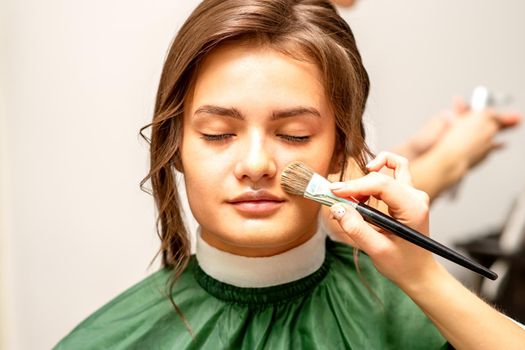 The makeup artist applies a cosmetic tonal foundation on the face using a makeup brush