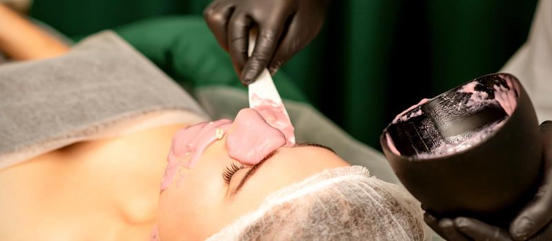 Beautiful young caucasian woman receiving an alginic mask to the face in beauty salon. Facial skin treatment