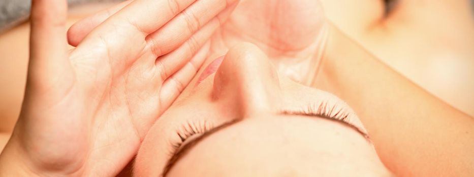 Beautiful caucasian young woman receiving a facial massage with closed eyes in spa salon, close up. Relaxing treatment concept