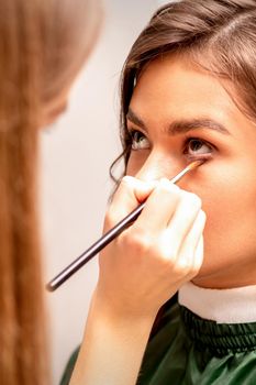 The makeup artist applies a concealer under the eyes using a makeup brush