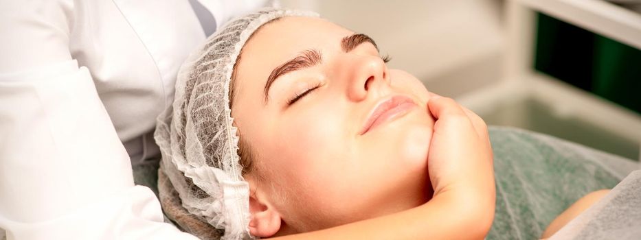 Facial massage. Hands of a masseur massaging neck of a young caucasian woman in a spa salon, the concept of health massage