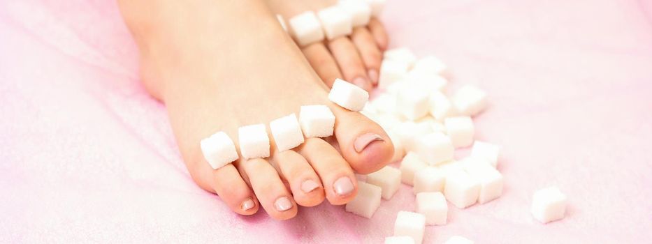 The concept of epilation, waxing. Sugar cubes lying down in a row on female feet, toes over pink background