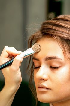 The makeup artist applies a cosmetic tonal foundation on the face using a makeup brush