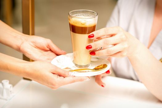 Barista serving coffee latte in glass mug for a customer, close up hands