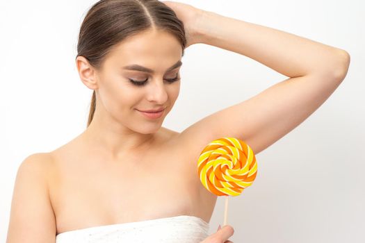 Waxing, depilation concept. The beautiful young caucasian woman covers her armpit with a lollipop on white background