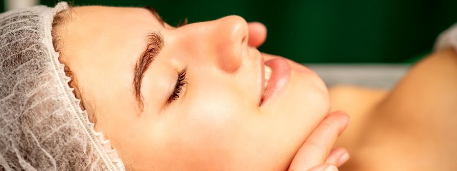 Facial massage. Hands of a masseur massaging neck of a young caucasian woman in a spa salon, the concept of health massage