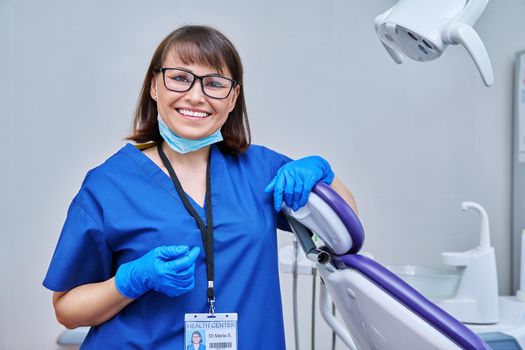 Portrait of smiling female doctor dentist in office. Confident middle aged woman looking at camera near dental chair. Dentistry, medicine, specialist, career, dental health care concept