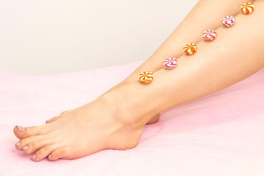 Depilation, waxing concept. Round candies lying down in a row on the female leg, close up