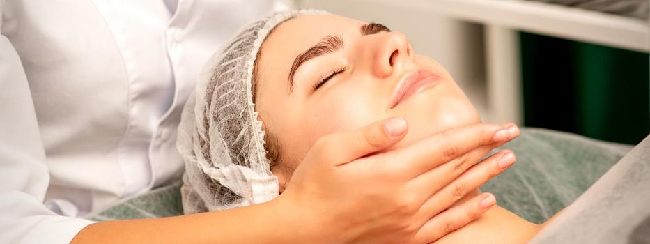 Facial massage. Hands of a masseur massaging neck of a young caucasian woman in a spa salon, the concept of health massage