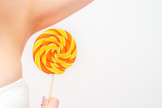 Waxing, depilation concept. A young female holds a round lollipop near her armpit on white background