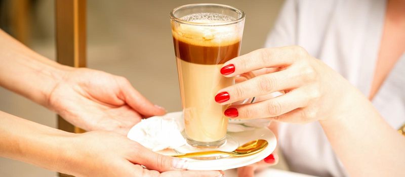 Barista serving coffee latte in glass mug for a customer, close up hands