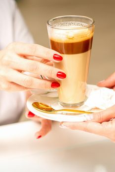 Barista serving coffee latte in glass mug for a customer, close up hands