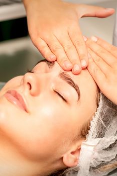 Head massage. Beautiful caucasian young white woman receiving a head and forehead massage with closed eyes in a spa salon