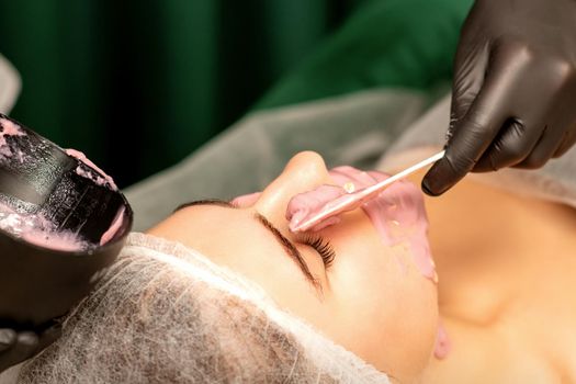 Beautiful young caucasian woman receiving an alginic mask to the face in beauty salon. Facial skin treatment