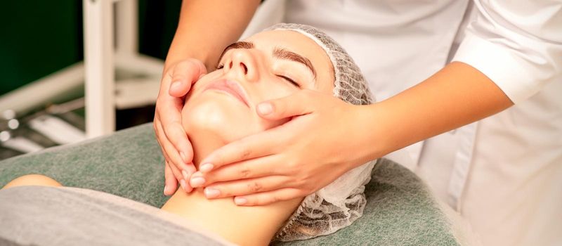 Facial treatment massage. Beautiful young caucasian woman with perfect skin receiving face and neck massage at a beauty spa