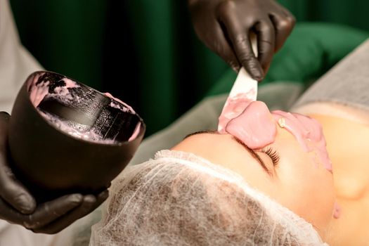 Beautiful young caucasian woman receiving an alginic mask to the face in beauty salon. Facial skin treatment