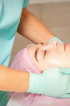 Cosmetologist with gloved hands applies a moisturizing mask with peeling cream on the female face. Facial cosmetology treatment. Procedures for facial care