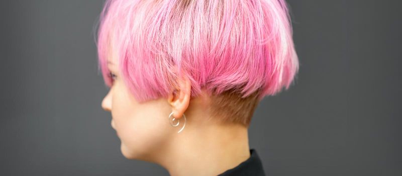 Profile of a beautiful young caucasian woman with short bob pink hairstyle on dark gray background