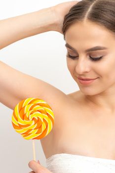 Waxing, depilation concept. The beautiful young caucasian woman covers her armpit with a lollipop on white background