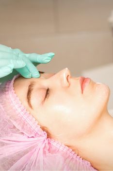 Cosmetologist with gloved hands applies a moisturizing mask with peeling cream on the female face. Facial cosmetology treatment. Procedures for facial care