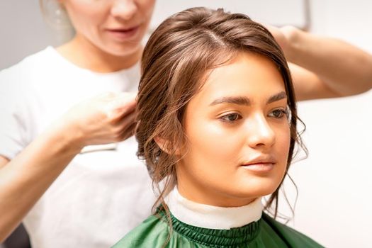 Hairstyling bride. A female hairdresser makes styling hair for the beautiful young caucasian woman in a beauty salon