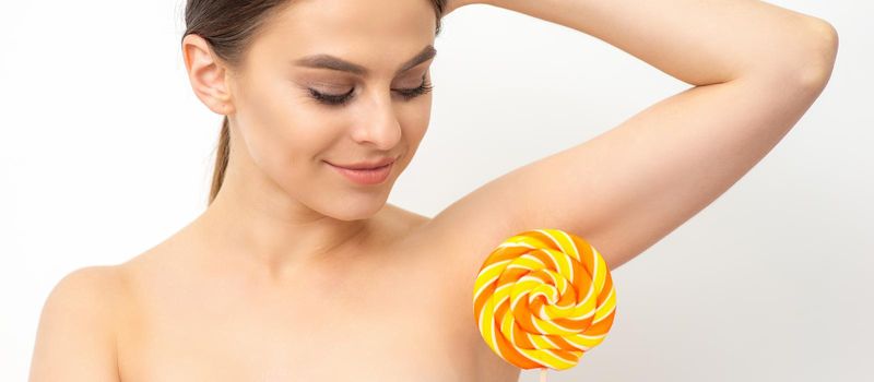 Waxing, depilation concept. The beautiful young caucasian woman covers her armpit with a lollipop on white background